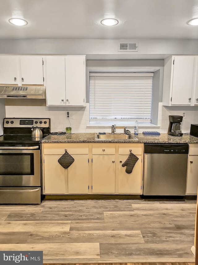 kitchen featuring dark stone countertops, stainless steel appliances, light wood-type flooring, range hood, and sink