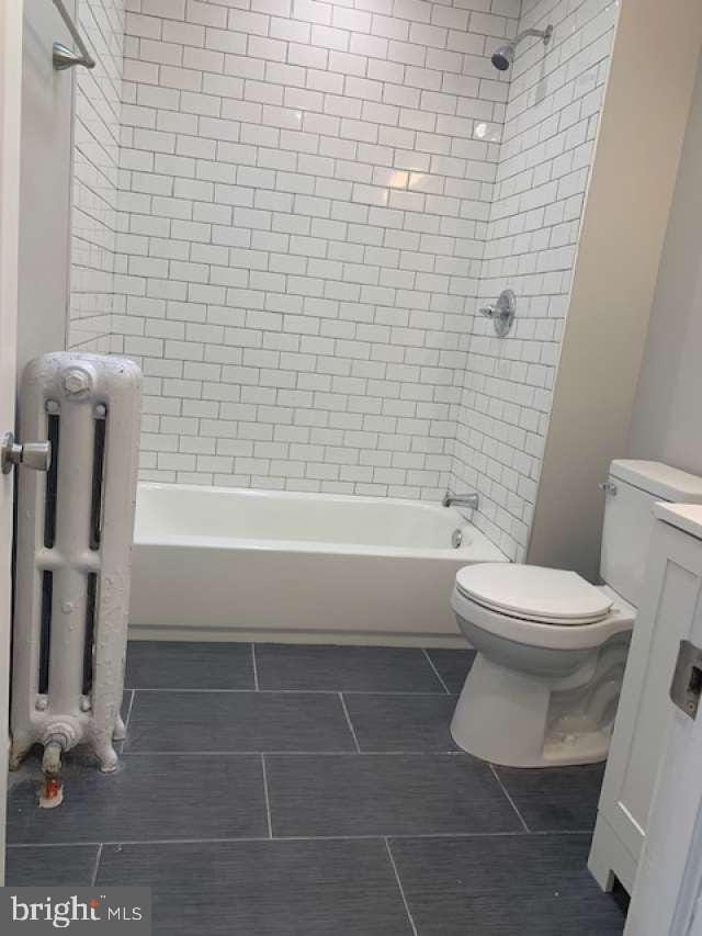 full bathroom with tiled shower / bath combo, vanity, toilet, and radiator heating unit