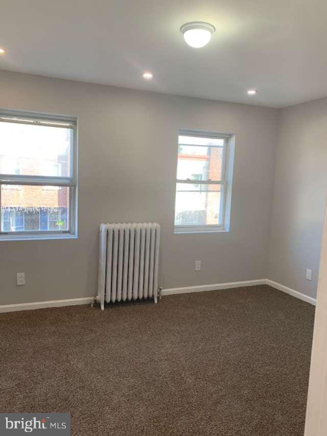 spare room featuring radiator and dark colored carpet