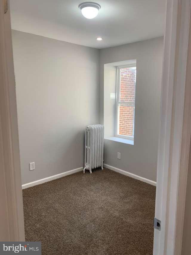 unfurnished room featuring radiator and dark carpet