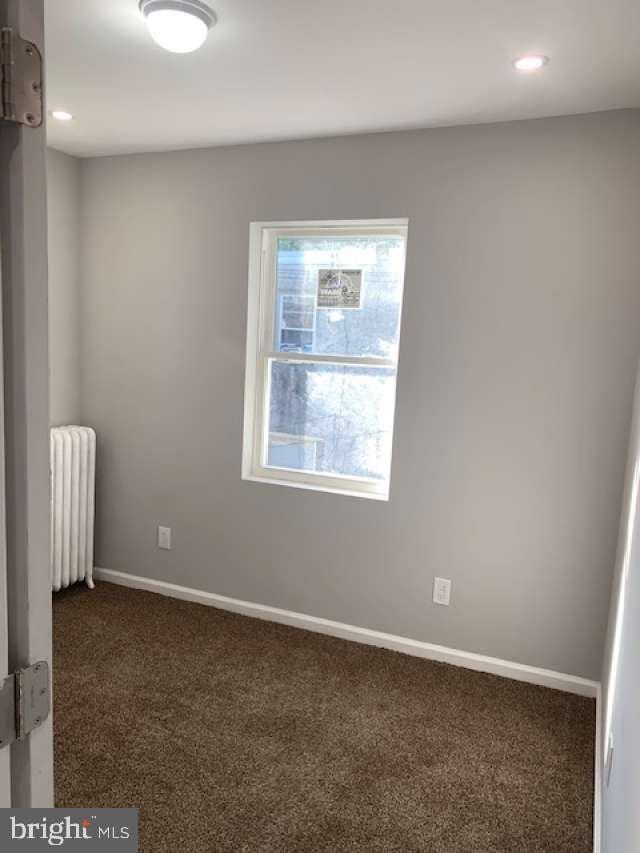 spare room featuring dark colored carpet and radiator heating unit