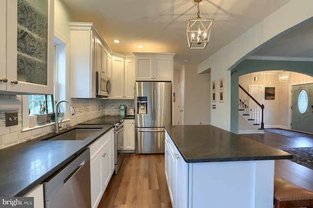 kitchen featuring backsplash, white cabinetry, appliances with stainless steel finishes, an inviting chandelier, and hardwood / wood-style floors