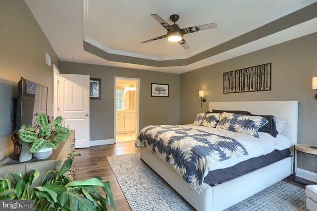 bedroom featuring a tray ceiling, dark wood-type flooring, ensuite bath, crown molding, and ceiling fan