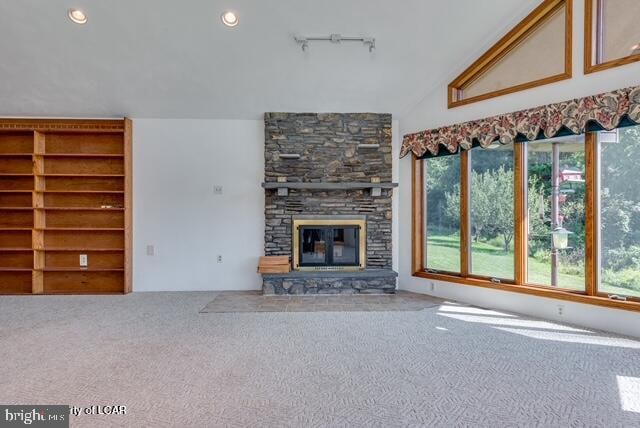 unfurnished living room featuring a stone fireplace, carpet flooring, and lofted ceiling