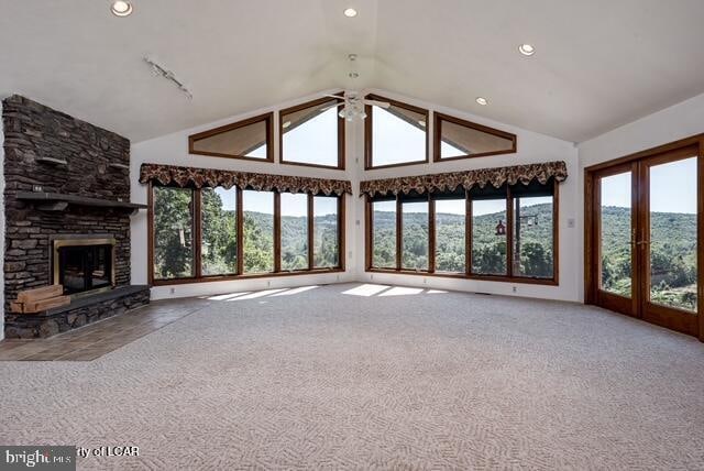 unfurnished living room with carpet floors, a stone fireplace, and vaulted ceiling