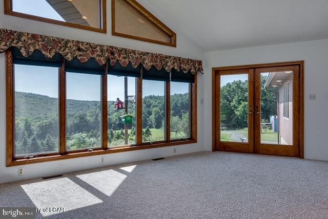 carpeted spare room featuring french doors, plenty of natural light, and vaulted ceiling