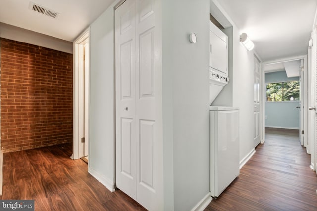 hallway featuring stacked washer / drying machine, dark hardwood / wood-style floors, and brick wall