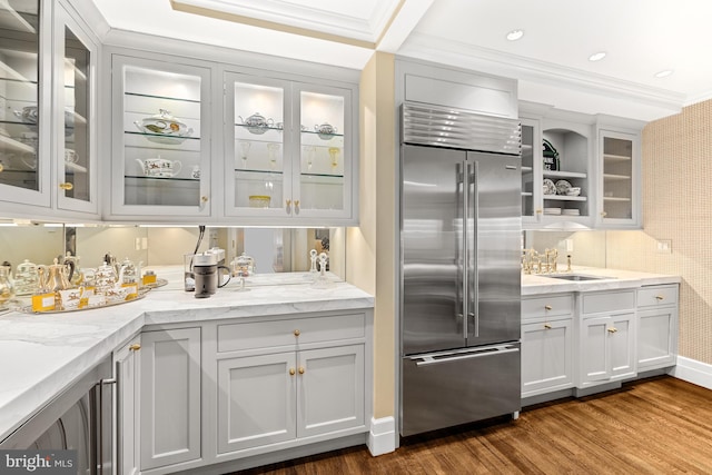 kitchen featuring light stone counters, ornamental molding, sink, built in refrigerator, and dark hardwood / wood-style flooring