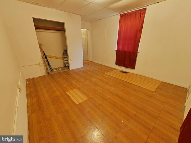 unfurnished bedroom with light wood-type flooring, a drop ceiling, and a closet