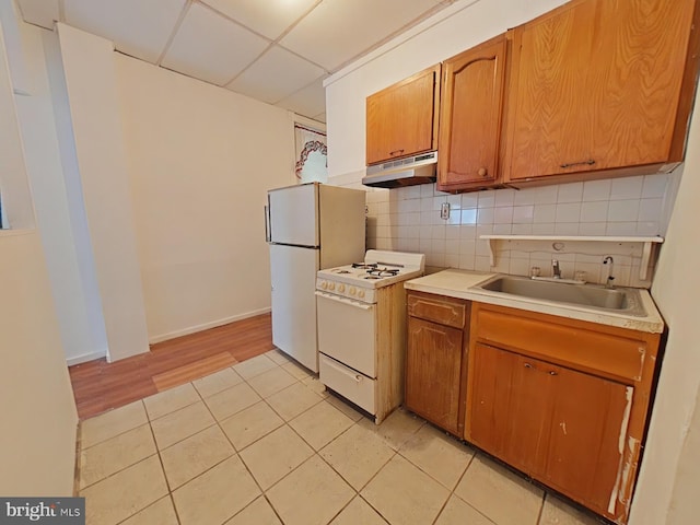 kitchen with sink, a drop ceiling, backsplash, white appliances, and light tile patterned floors