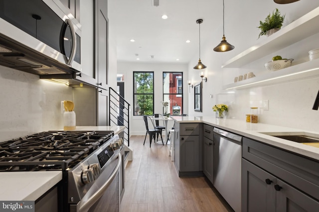 kitchen with kitchen peninsula, decorative light fixtures, gray cabinets, appliances with stainless steel finishes, and light hardwood / wood-style floors