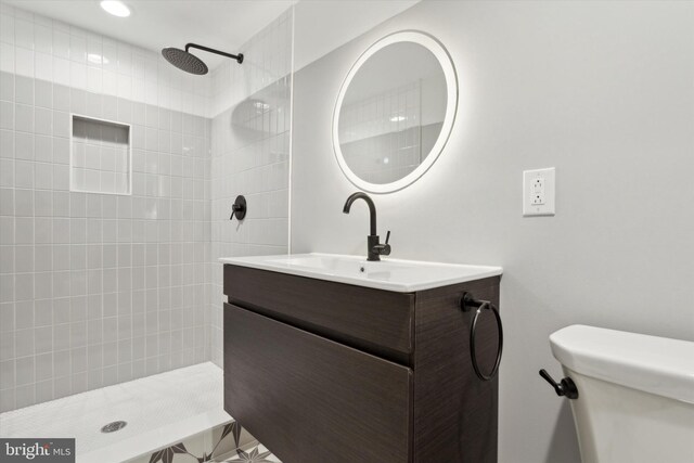 bathroom with a tile shower, vanity, and toilet