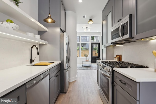 kitchen featuring appliances with stainless steel finishes, hanging light fixtures, gray cabinetry, light wood-type flooring, and sink