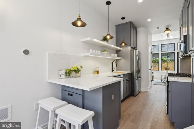 kitchen featuring a kitchen bar, decorative light fixtures, stainless steel appliances, and kitchen peninsula