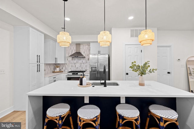 kitchen featuring appliances with stainless steel finishes, hanging light fixtures, a center island with sink, and wall chimney range hood