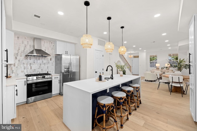 kitchen with pendant lighting, wall chimney range hood, white cabinetry, appliances with stainless steel finishes, and light hardwood / wood-style floors