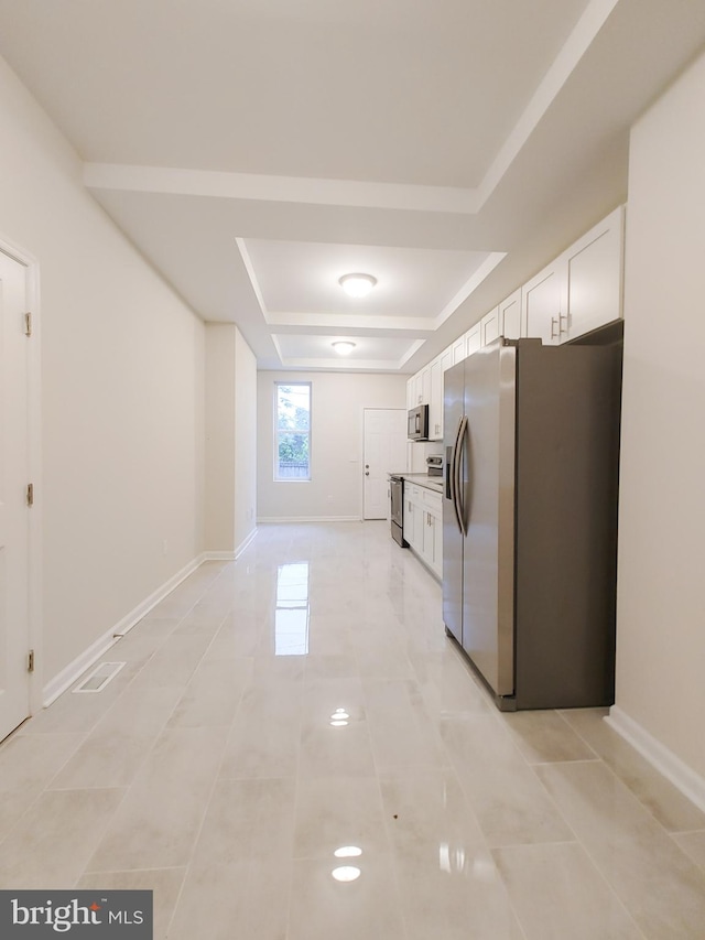 kitchen featuring light tile patterned flooring, a tray ceiling, stainless steel appliances, and white cabinets