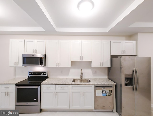 kitchen featuring a raised ceiling, sink, white cabinetry, appliances with stainless steel finishes, and light stone countertops