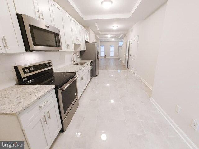 kitchen with light stone countertops, stainless steel appliances, white cabinets, and sink