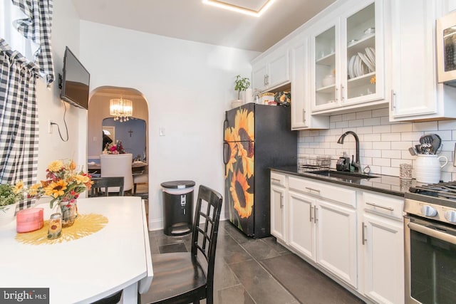 kitchen featuring decorative backsplash, white cabinetry, black refrigerator, sink, and a notable chandelier