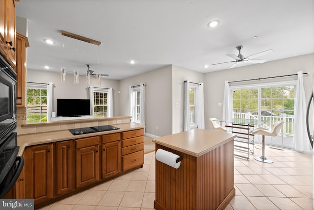 kitchen with ceiling fan, hanging light fixtures, light tile patterned floors, a kitchen island, and black appliances