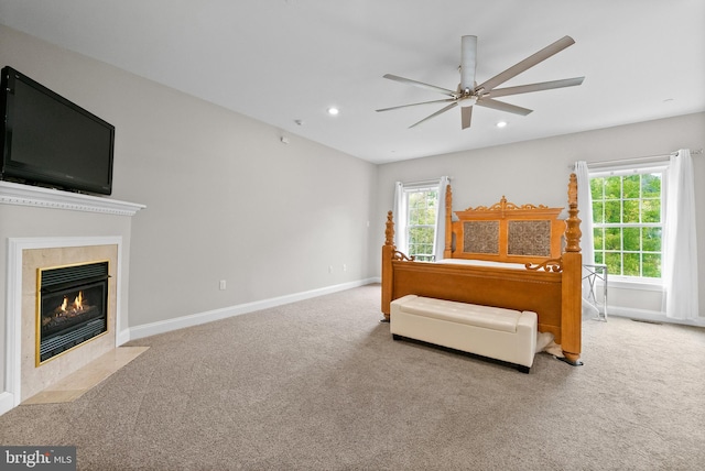 bedroom featuring a tiled fireplace, ceiling fan, and light colored carpet