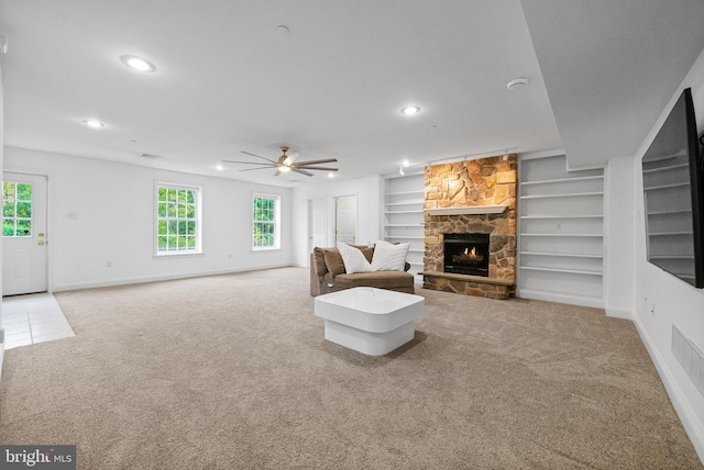 living room featuring light carpet, built in shelves, ceiling fan, and a stone fireplace