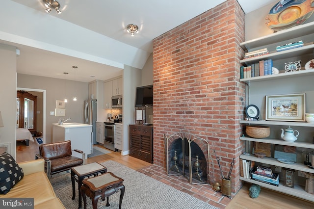 living room featuring a brick fireplace, vaulted ceiling, light hardwood / wood-style floors, and sink