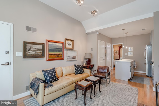 living room with vaulted ceiling, light hardwood / wood-style floors, and sink