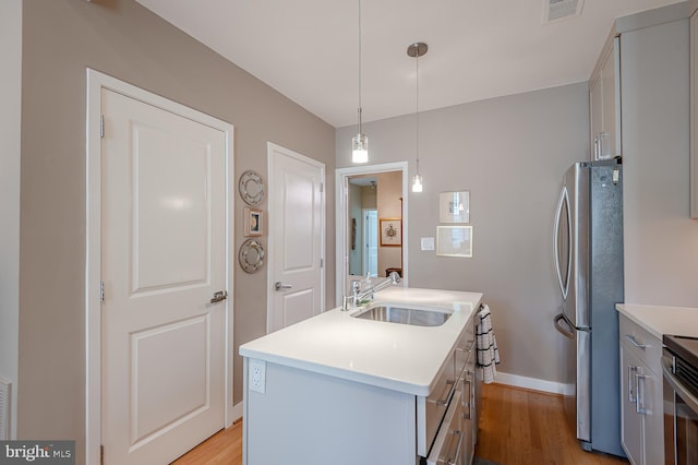 kitchen with hanging light fixtures, an island with sink, stainless steel appliances, light wood-type flooring, and sink