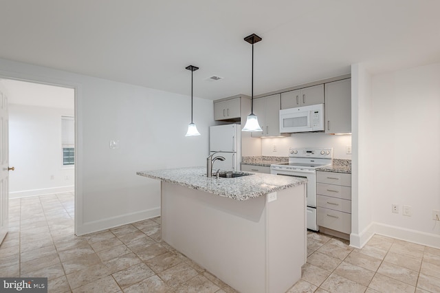 kitchen featuring pendant lighting, an island with sink, sink, white appliances, and light stone countertops