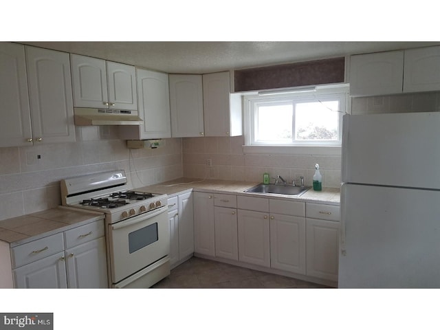 kitchen featuring dark tile patterned floors, white cabinets, white appliances, and sink