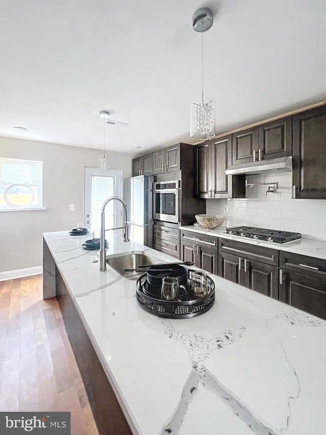 kitchen featuring light stone countertops, appliances with stainless steel finishes, decorative light fixtures, and tasteful backsplash