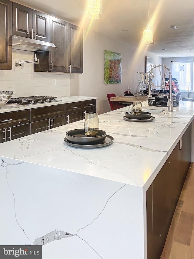 kitchen with decorative backsplash, light stone counters, and stainless steel gas cooktop