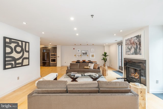 living area with a fireplace with flush hearth, recessed lighting, light wood-style flooring, and baseboards