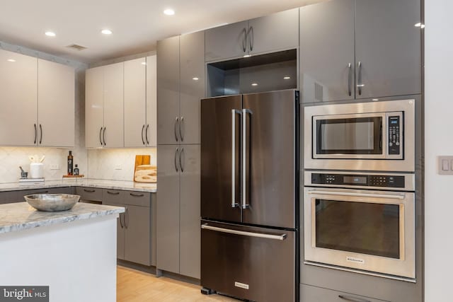 kitchen with tasteful backsplash, light stone counters, gray cabinets, stainless steel appliances, and light wood-type flooring