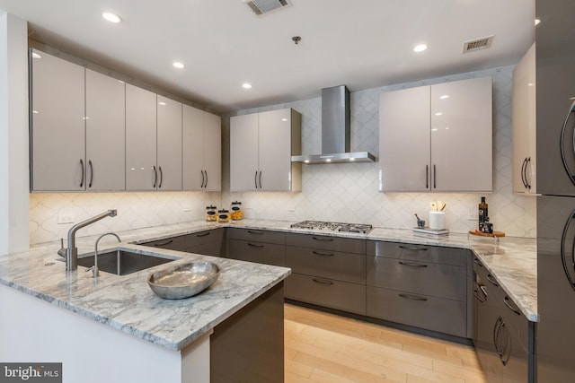 kitchen with gray cabinets, visible vents, a sink, and wall chimney range hood