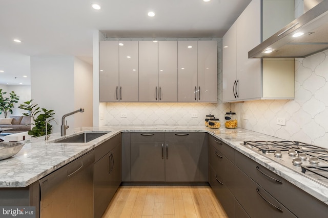 kitchen with a peninsula, a sink, exhaust hood, appliances with stainless steel finishes, and light wood finished floors