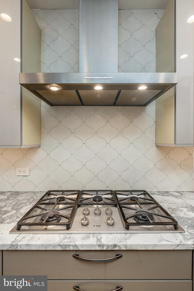 kitchen with light stone countertops, stainless steel gas cooktop, decorative backsplash, and exhaust hood