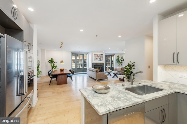 kitchen featuring decorative backsplash, appliances with stainless steel finishes, gray cabinets, a fireplace, and a sink