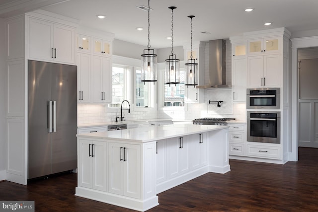 kitchen with stainless steel appliances, dark wood-type flooring, a center island, and wall chimney range hood