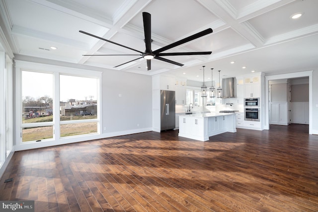 kitchen featuring ceiling fan, an island with sink, decorative light fixtures, wall chimney exhaust hood, and dark wood-type flooring