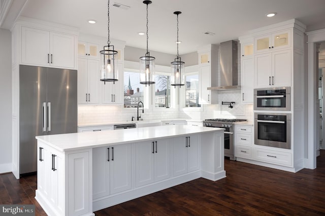 kitchen with a kitchen island, premium appliances, wall chimney exhaust hood, white cabinetry, and dark hardwood / wood-style floors