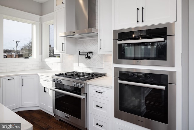 kitchen with white cabinetry, dark wood-type flooring, tasteful backsplash, wall chimney exhaust hood, and stainless steel appliances