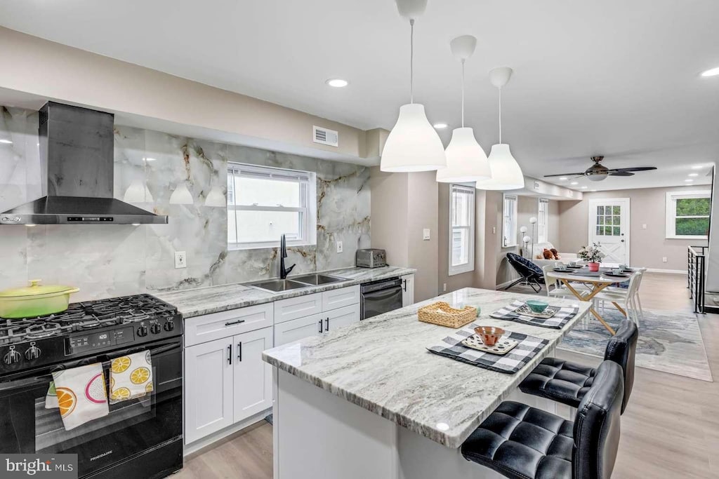 kitchen featuring white cabinetry, wall chimney exhaust hood, black appliances, ceiling fan, and sink