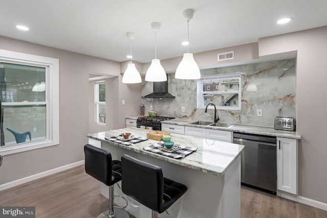 kitchen with white cabinets, wall chimney exhaust hood, pendant lighting, stainless steel dishwasher, and sink