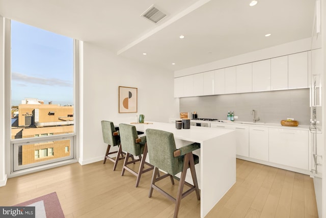 kitchen with kitchen peninsula, white cabinetry, and light hardwood / wood-style flooring