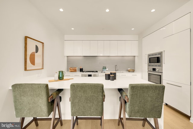 kitchen with a kitchen breakfast bar, light wood-type flooring, stainless steel appliances, built in desk, and white cabinets