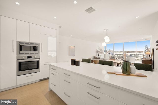 kitchen featuring hanging light fixtures, white cabinets, stainless steel appliances, and light hardwood / wood-style floors