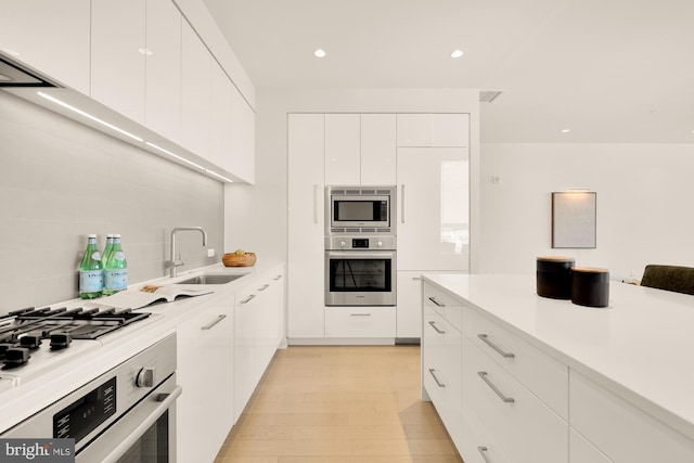 kitchen with sink, white cabinets, stainless steel appliances, and light hardwood / wood-style floors